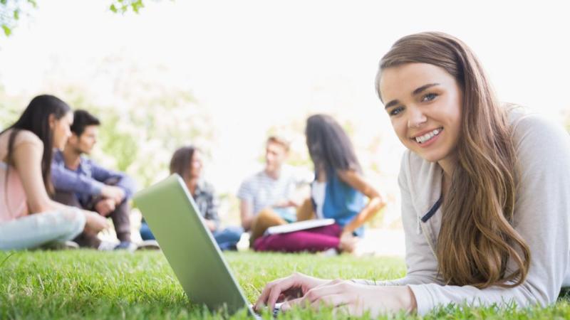 female student on laptop lying on grass